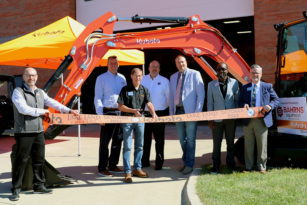 Pictured are Manager of Educational Partnerships for Kubota Jeff Wagley, Vice President for Business Services Greg Nuxoll, Ag Power Technology Instructor Woody Reinhart, Kubota Corporate Leadership Midwest Division Matt Dugan, Division Chair Agriculture/Agriculture Instructor Ryan Orrick, Vice President for Academic Services Ike Nwosu and Lake Land College President Josh Bullock standing posed with a Kubota tractor with Reinhart poised to cut an orange ribbon while Wagley and Bullock hold the left and right ends respectively